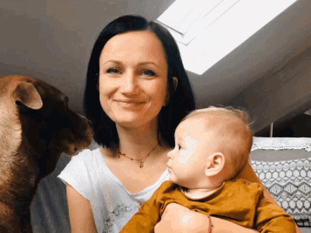 a woman is holding a baby and a dog looks on