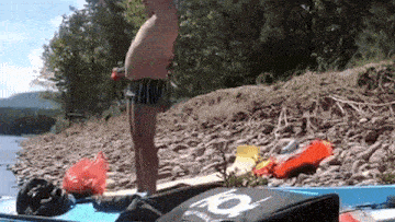 a man is standing on a paddle board on the shore of a river .