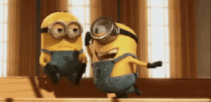 two minions wearing goggles are standing next to each other on a wooden table .