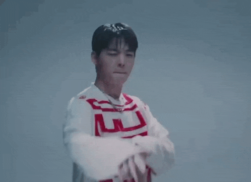 a young man wearing a white and red sweater is standing with his arms crossed and looking at the camera .