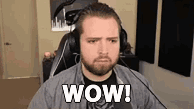 a man with a beard and headphones is sitting in front of a microphone and saying wow .