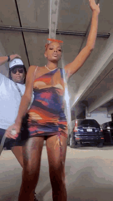 a woman in a dress is dancing in a parking garage with a man behind her