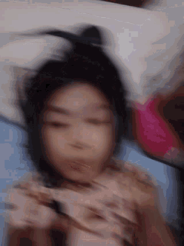 a blurry picture of a person laying on a bed with their head on a pillow .