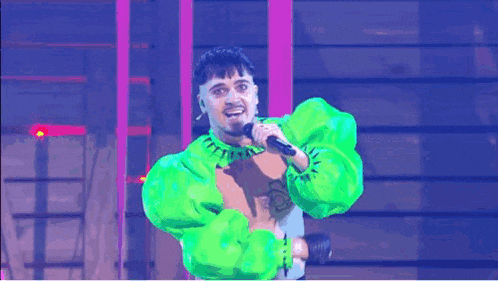 a man in a neon green outfit is singing into a microphone on stage .