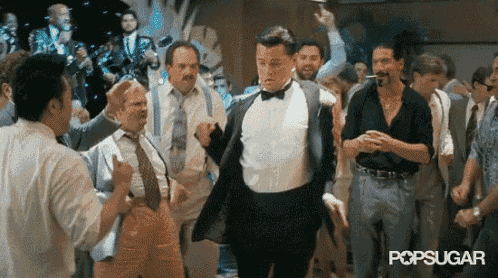 a man in a tuxedo is dancing with a group of men in suits .
