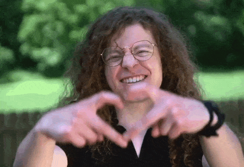 a young man with curly hair is making a heart shape with his hands .