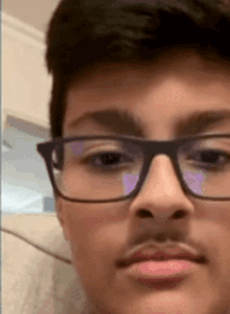 a young boy with glasses and a mustache is looking at the camera .
