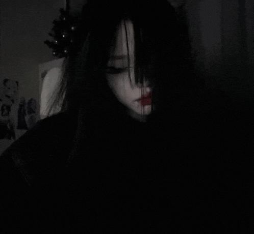 a girl with long black hair is covering her face with her hair in a dark room .
