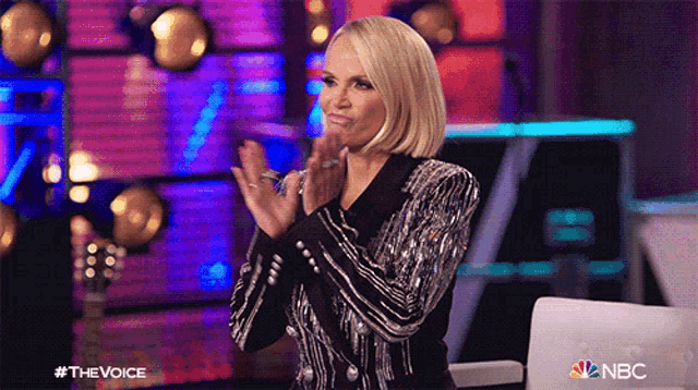 a woman applauds while wearing a black and silver jacket