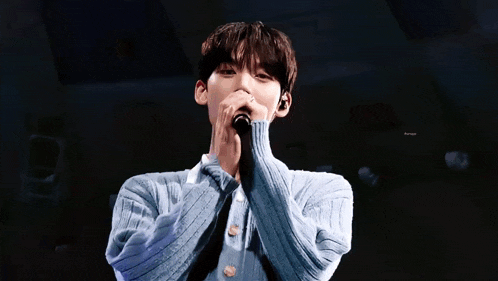 a young man is singing into a microphone on stage .
