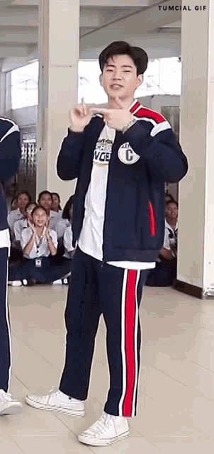 a boy in a blue and red tracksuit is standing in front of a group of people .