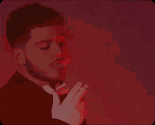a man in a suit and tie is smoking a cigarette in front of a red and yellow background