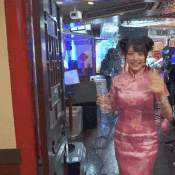 a woman in a pink dress is walking through a doorway while holding a drink .
