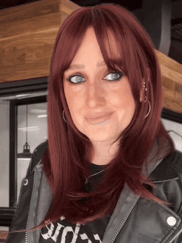 a woman with red hair is wearing a leather jacket and a black shirt that says riot