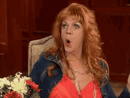 a woman with red hair is sitting in a chair with flowers in front of her