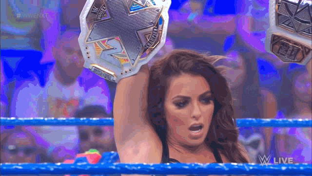 a woman in a wrestling ring holds up a championship belt