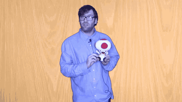 a man in a blue shirt is holding a stuffed toad with a red spot on his head