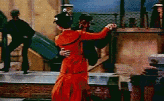 a woman in an orange dress dancing with a man in a black hat