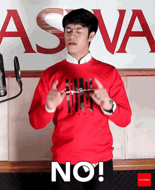 a man wearing a red sweater says no in front of a sign that says asva
