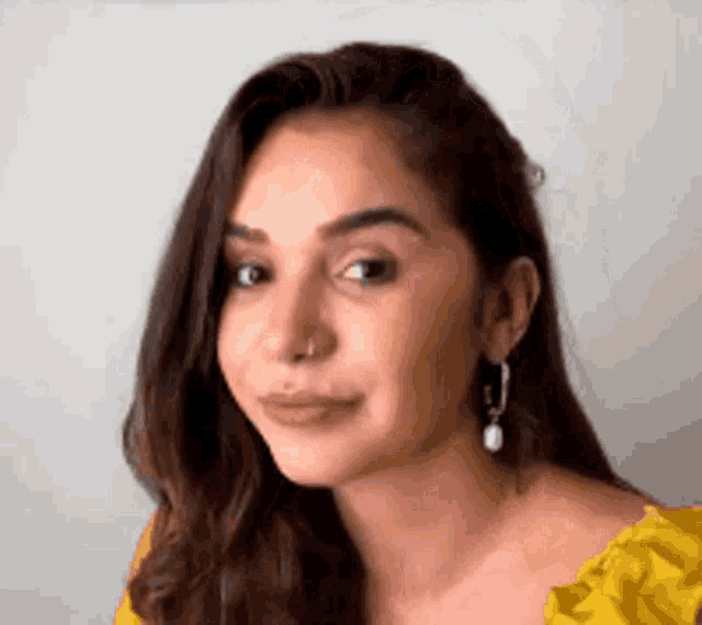 a close up of a woman wearing a yellow top and earrings .