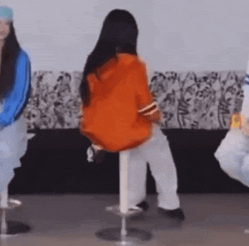 a woman is sitting on a bar stool while a group of people are dancing .
