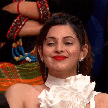 a woman wearing a white dress and red lipstick is smiling and looking at the camera .