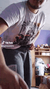 a man wearing a white shirt with a motorcycle on it is standing in a bedroom