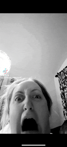 a black and white photo of a woman making a funny face with her mouth open .