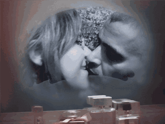 a couple kissing in front of a mirror with perfume bottles in the background