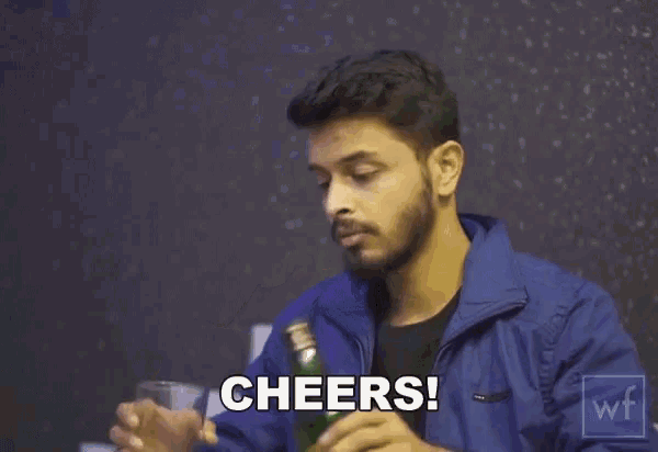 a man in a blue jacket is drinking from a bottle and says cheers !