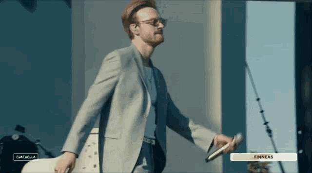 a man in a suit and sunglasses holds a microphone in front of a screen that says finneas
