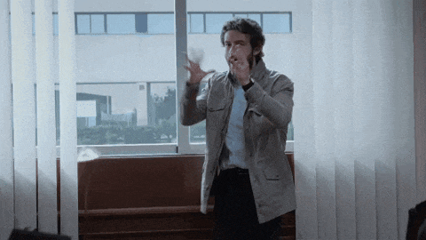 a man in a grey jacket is standing in front of a window with blinds