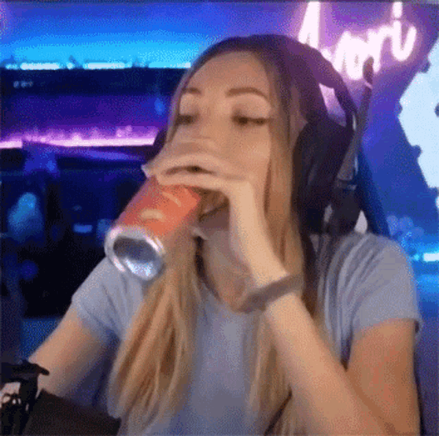 a woman wearing headphones is drinking from a can while playing a video game .