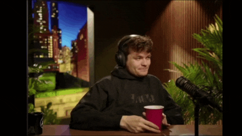 a man wearing headphones is holding a red cup in front of a microphone ..