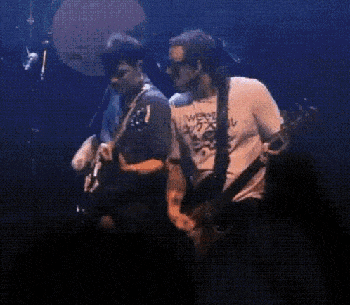 two men are playing guitars on a stage and one of them is wearing a shirt that says weed