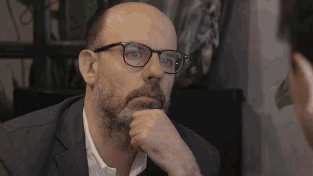 a bald man with glasses and a beard looks serious