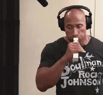 a man wearing headphones and a rock johnson t-shirt is holding a microphone .