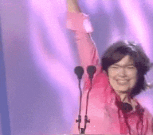 a woman in a pink shirt is standing in front of a podium with her arm in the air .