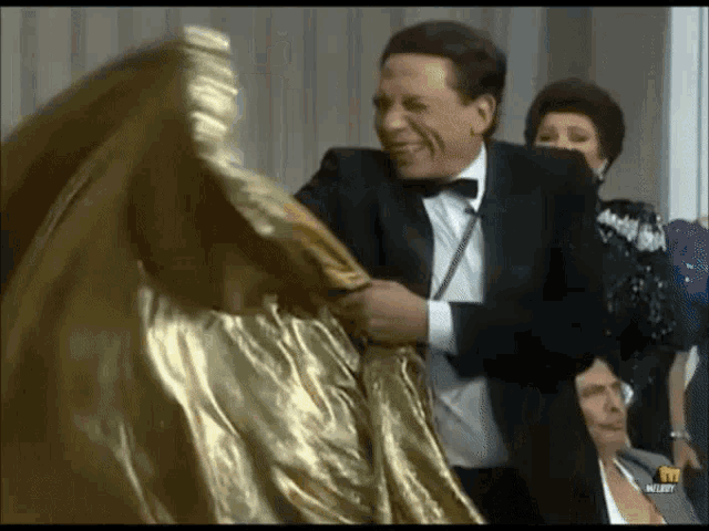 a man in a tuxedo and bow tie is holding a gold dress