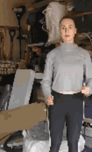 a woman in a grey sweater and black pants is standing in a garage with a suitcase .