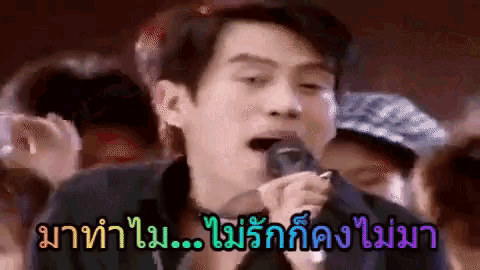 a man is singing into a microphone in front of a crowd with foreign writing on the bottom