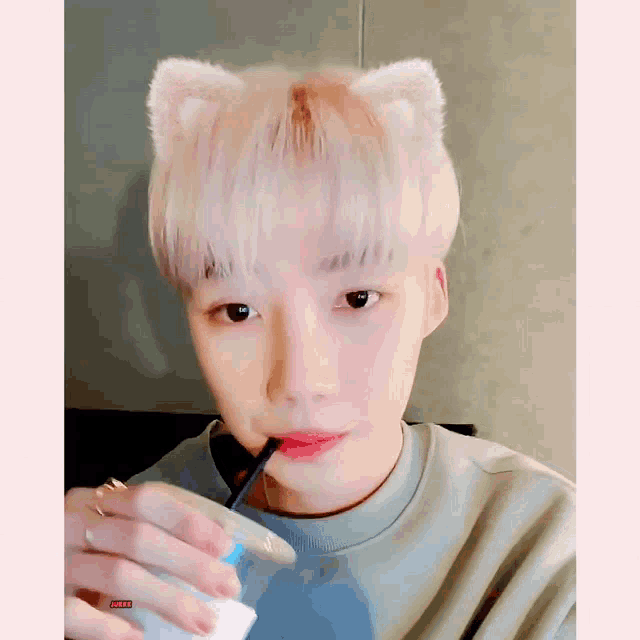 a young man with cat ears is drinking through a straw from a cup .