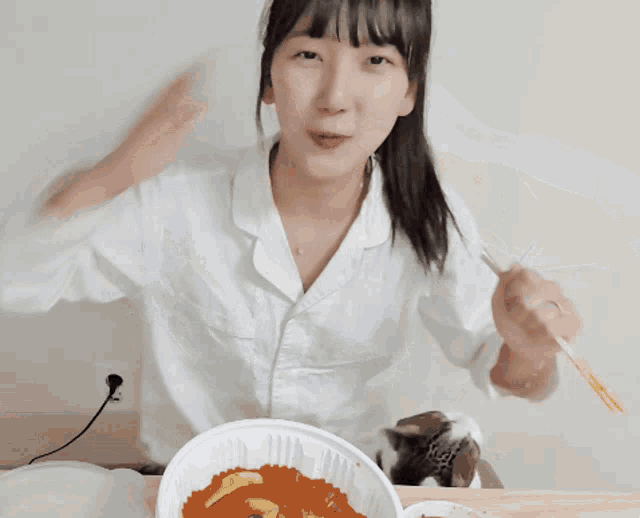 a woman in a white shirt is eating a bowl of food with a fork