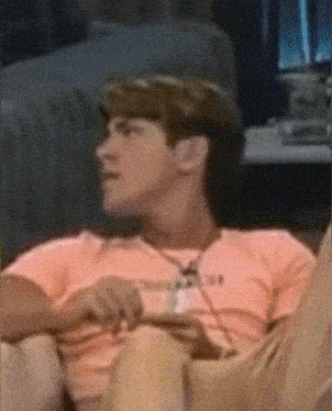 a man sitting on a couch with a pink shirt on