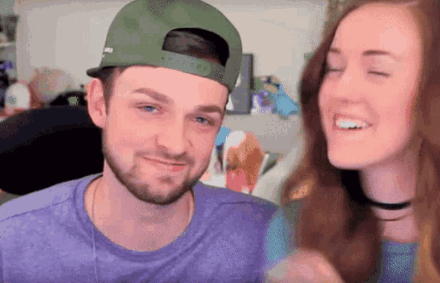a man and a woman are laughing together and the man is wearing a green hat that says mlb on it