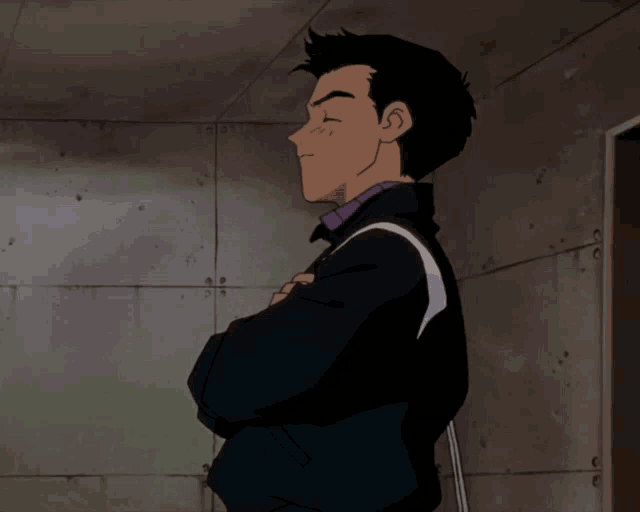 a man in a black jacket stands with his arms crossed in front of a wall