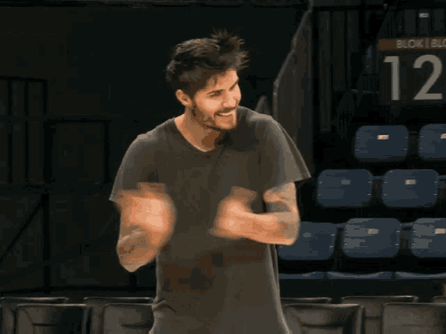 a man in a grey shirt is clapping his hands and smiling