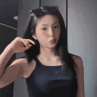 a young woman wearing sunglasses and a black tank top is looking at herself in the mirror .