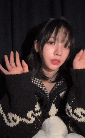 a young woman wearing a black and white sweater is waving her hands in the air .