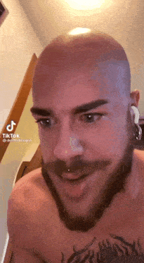 a bald man with a beard and piercings on his ears .